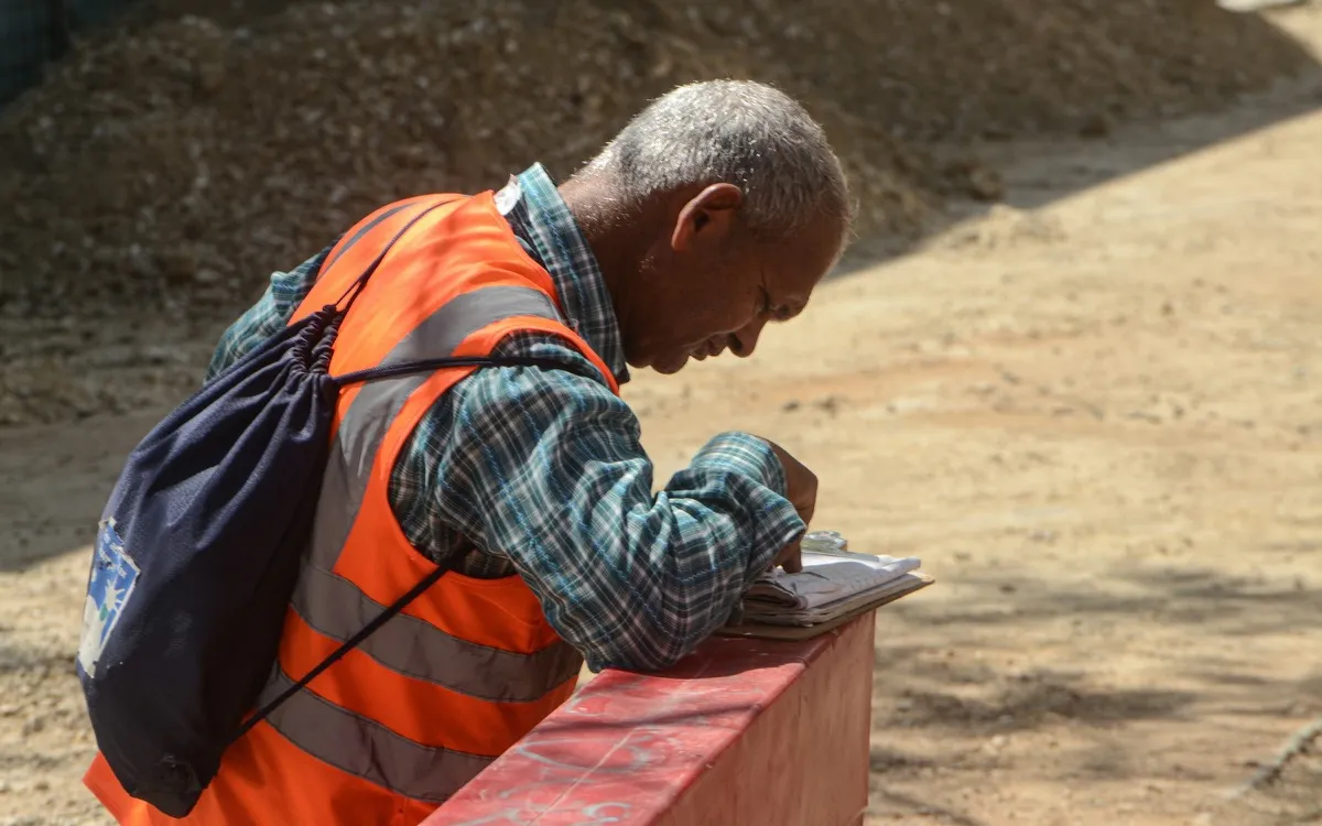 A site worker filling in a paper timesheet on a block of concrete