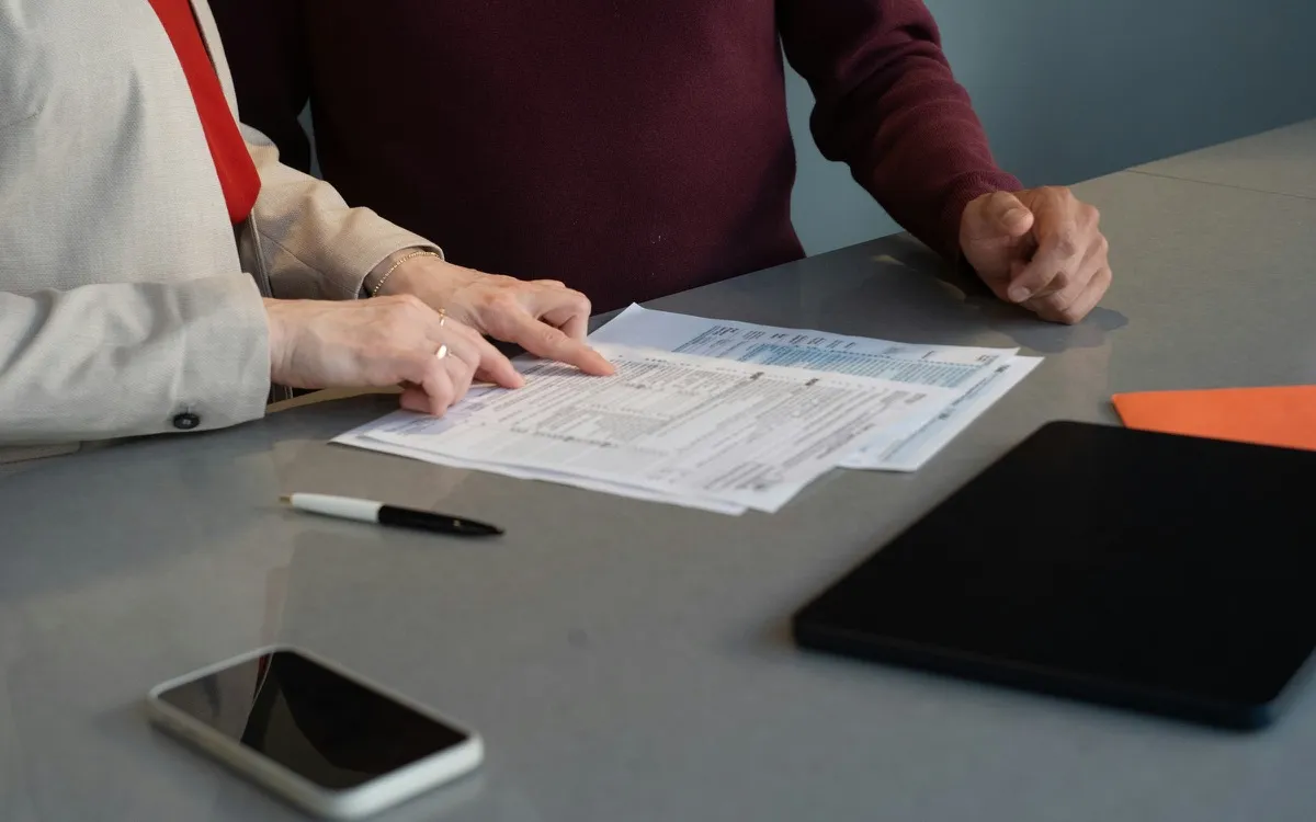 One person pointing out a line on a printed policy schedule to another across a desk