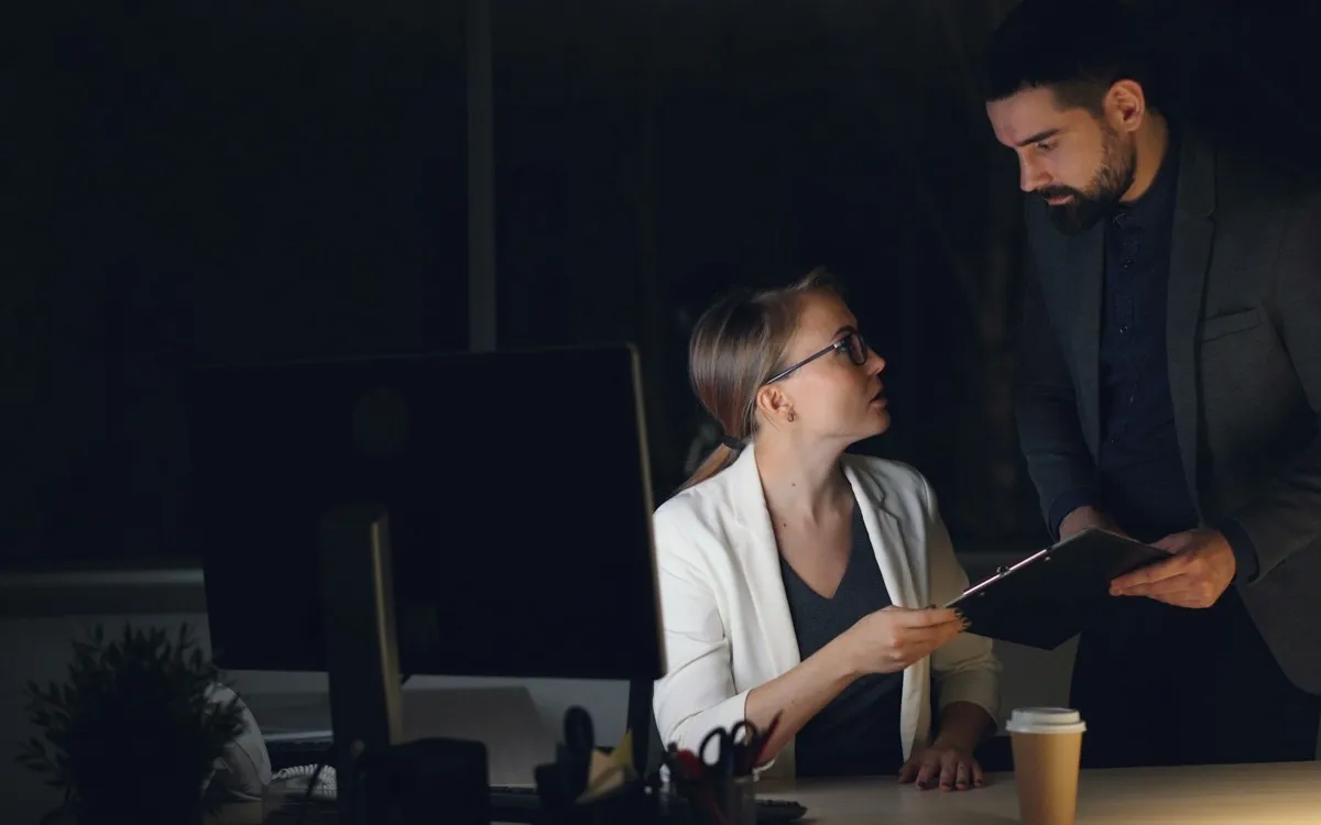 A manager handing a clipboard across a desk for sign-off, late in the office